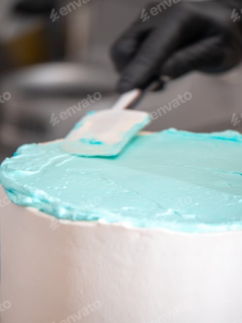 Preview: cake designer covering a frosted blank cake with turquoise light blue cream with spatula