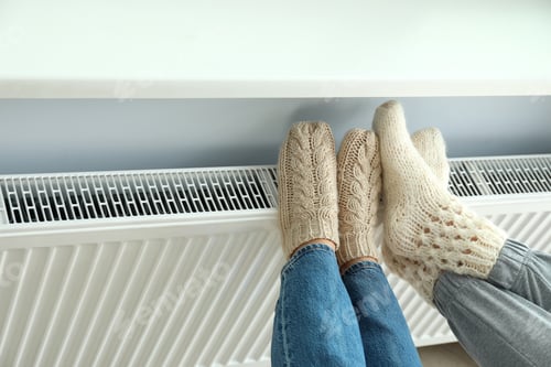 Preview: Concept of heating season with legs in knitted boots on radiator