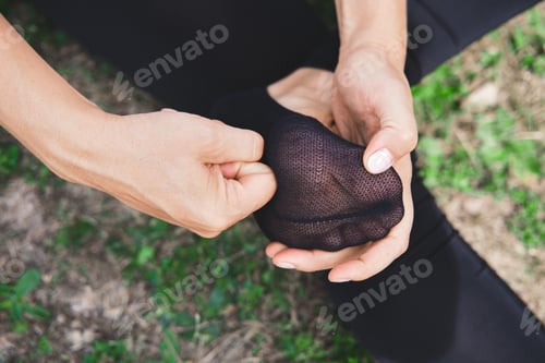 Preview: Woman sitting on grass and massages the foot in sock close-up. Pain or cramping in the foot.