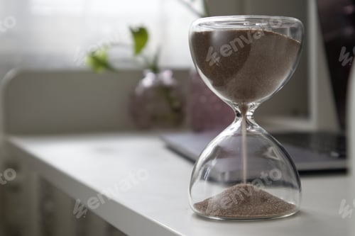 Preview: Hourglass on a white table against the background of an open laptop close-up