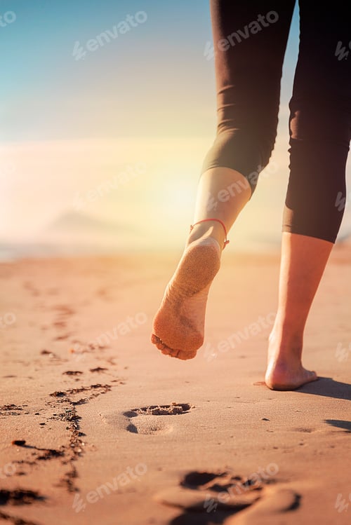 Preview: legs of woman walking on sand of beach marking her footprints as she walks away