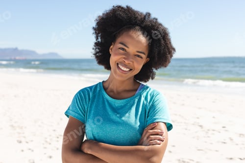Preview: Portrait of happy african american woman looking at camera and smiling sunny on beach