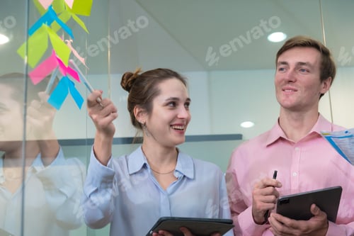 Preview: Team meeting professionals engaged in brainstorming with colorful sticky notes on glass wall.
