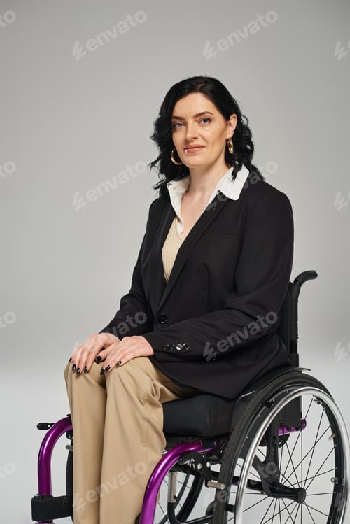Preview: cheerful attractive disabled woman in black chic blazer sitting in wheelchair and smiling at camera