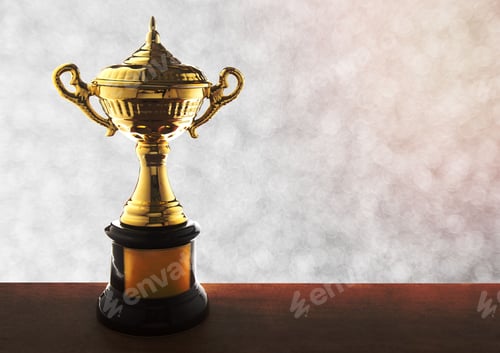 Preview: Golden trophy atop a wooden tabletop with an abstract white bokeh background