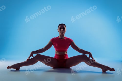 Preview: Woman doing seated straddle stretch for hip opening and inner thigh flexibility on blue background