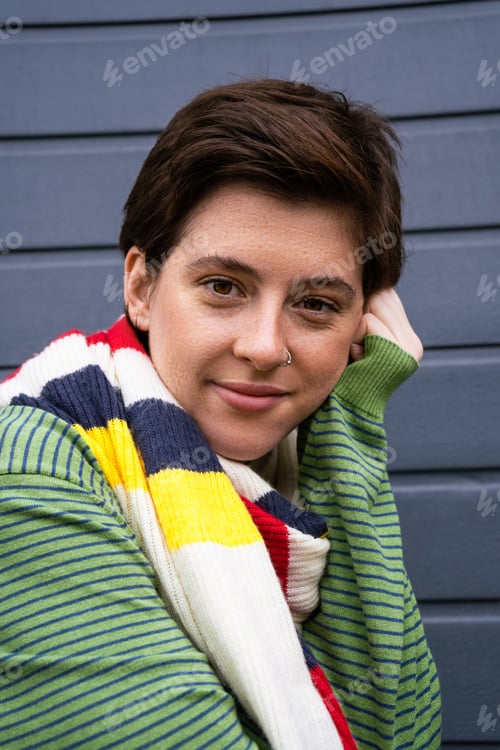 Preview: portrait of carefree freckled woman in striped multicolored scarf looking at camera near grey wall