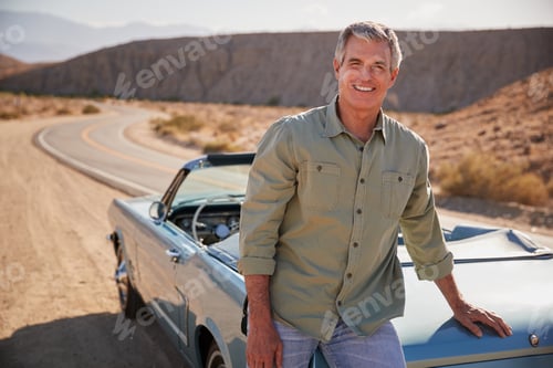 Preview: Senior white man leaning on open top car at desert roadside