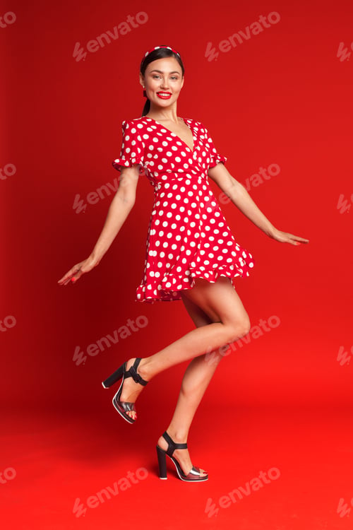 Preview: Fashion model poses in bright red polka dot dress against a bold red backdrop