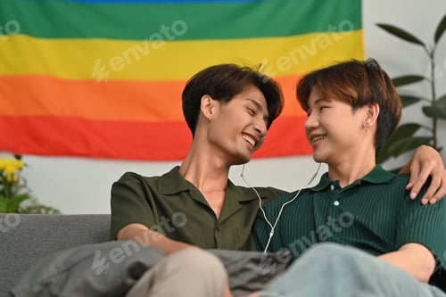 Preview: Carefree male gay couple listening to music on earphones, spending time together at home.