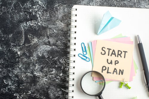 Preview: top view start up plan note on sticker with pen and magnifier on gray background lesson student