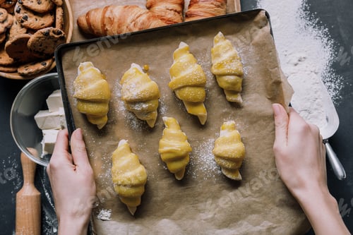 Preview: partial view of woman holding tray with dough for croissants over table ingredients