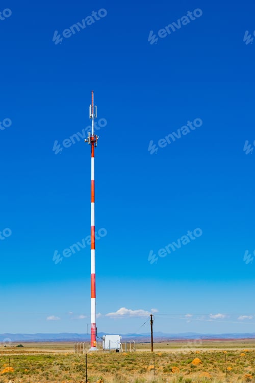 Preview: Vertical shot of a striped cell phone tower in the countryside of South Africa under a blue sky