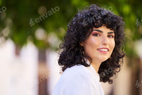 Preview: A woman with curly hair is smiling and wearing a white shirt