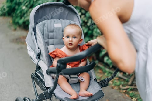 Preview: Portrait of a baby sitting in a stroller with her mother leaning towards her during a walk.