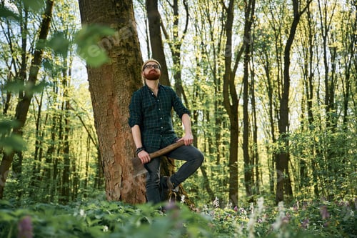 Preview: Holding an axe. Bearded man is in the forest at daytime