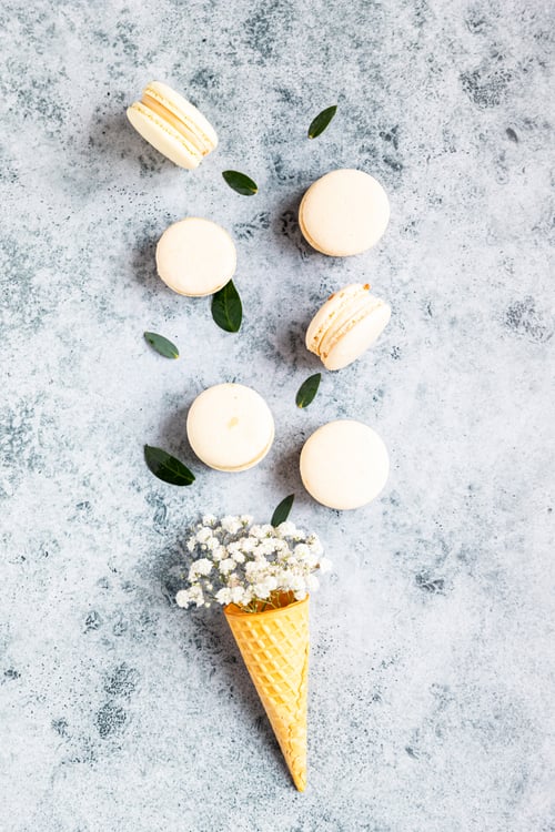 Preview: Waffle cone filled with gypsophila flowers and macarons with leaves on grey background.