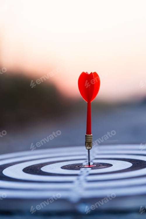Preview: Close up red dart arrow hitting target center dartboard on sunset background. Business targeting and