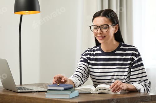 Preview: Young woman with laptop studying at table in library
