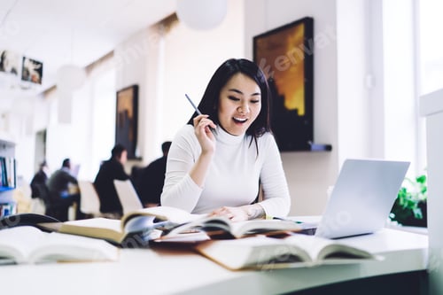 Preview: Elegant adult ethnic woman rejoicing breakthrough while sitting at laptop with notepad
