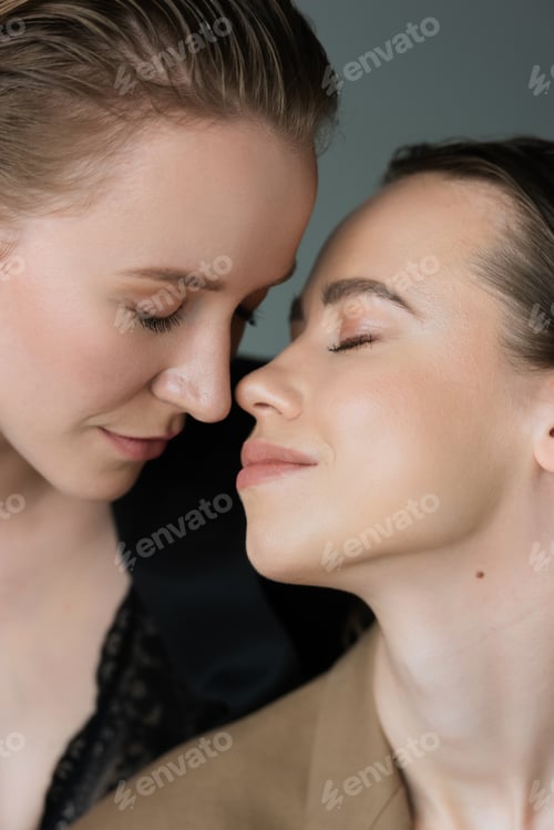 Preview: young lesbian couple smiling face to face with closed eyes isolated on grey