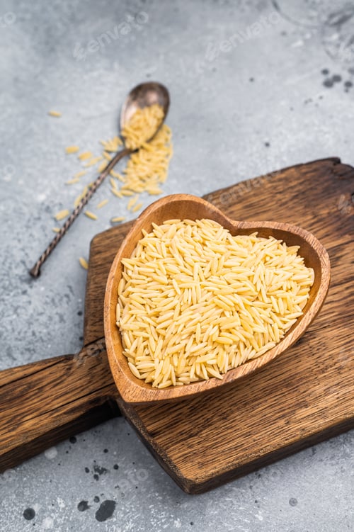 Preview: Raw Orzo pasta, uncooked dry Italian risoni in a bowl. grey background. top view