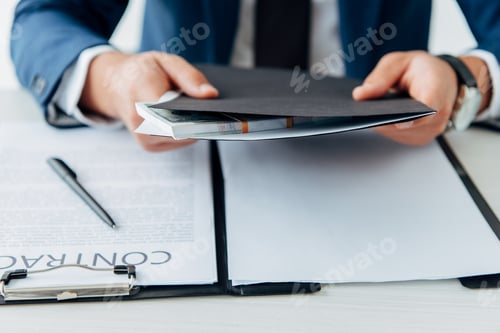 Preview: selective focus of man holding folder with money near contract with pen