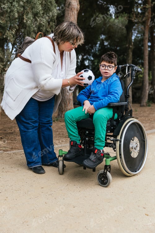 Preview: A mother giving a soccer ball to her son with a disability who uses a wheelchair in the park to play