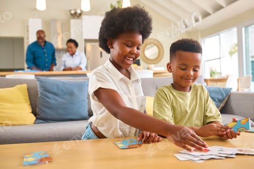 Preview: Boy And Girl Playing Game Of Cards At Home With Multi Generation Family In Background