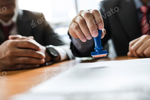 Preview: Businessman stamping with approved stamp on document at meeting.