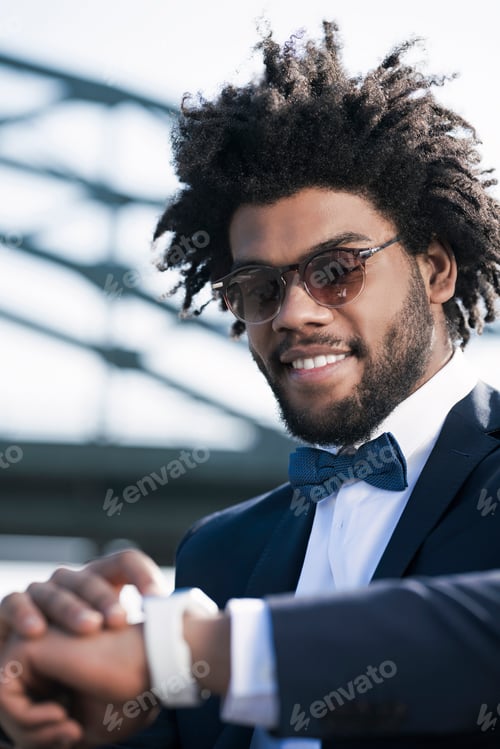 Preview: Smiling young man with sunglasses looking at his smartwatch