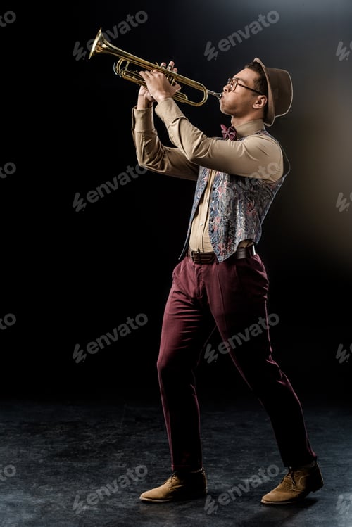 Preview: young mixed race male jazzman in hat playing on trumpet on black