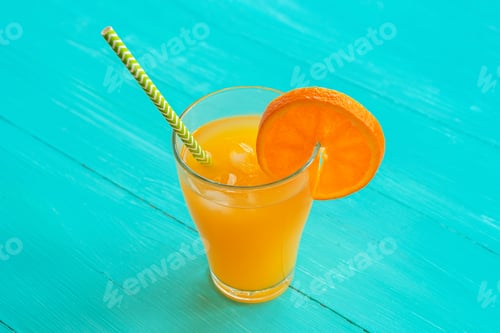 Preview: Orange juice with ice and straw in a glass on turquoise blue wooden table, top view