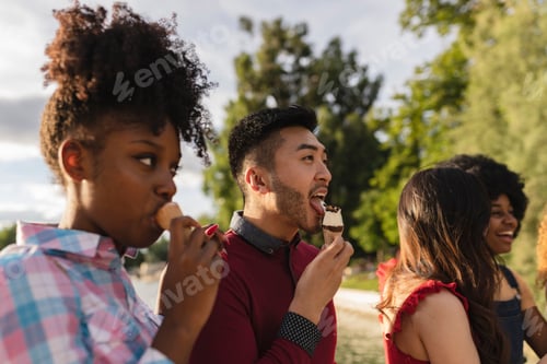 Preview: multiracial adult friends eat ice cream in the park in summer - focus on asian man -