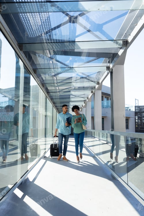 Preview: Full length of african american colleagues discussing while walking with luggage at airport corridor