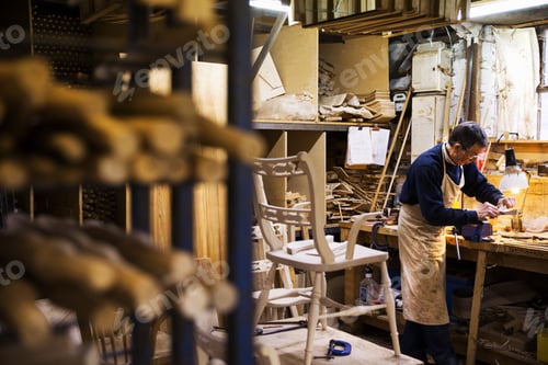 Preview: Man standing at a work bench in a carpentry workshop, working on a piece of wood secured in a bench