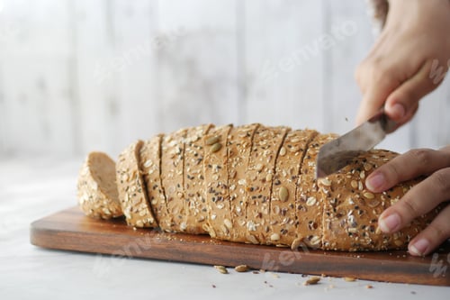 Preview: Women hand cutting baked brow bread on table.
