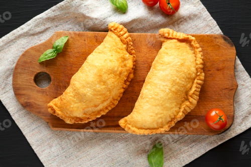 Preview: Homemade Deep Fried Italian Panzerotti Calzone on a rustic wooden board on a black background