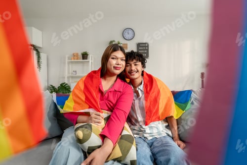 Preview: Portrait of transgender woman and partner holding rainbow flag in house.