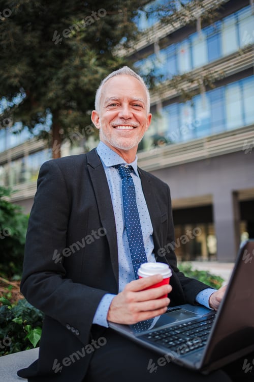 Preview: Vertical. Mature businessman in suit using a laptop computer sitting outside the office, relaxing