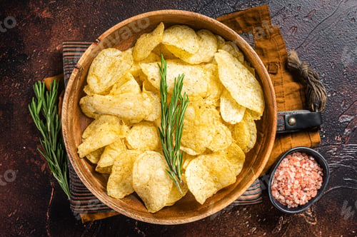 Preview: Homemade potato chips with sea salt and rosemary in wooden plate. Dark background. Top view