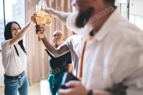 Preview: Diverse company toasting beer bottles in brightly lit apartment