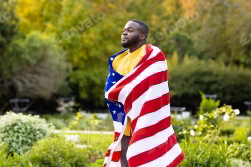 Preview: Happy african american man covered with flag of usa in garden