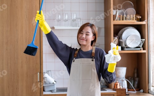 Preview: A woman wearing protective glove, holding a broom and dancing while cleaning at home