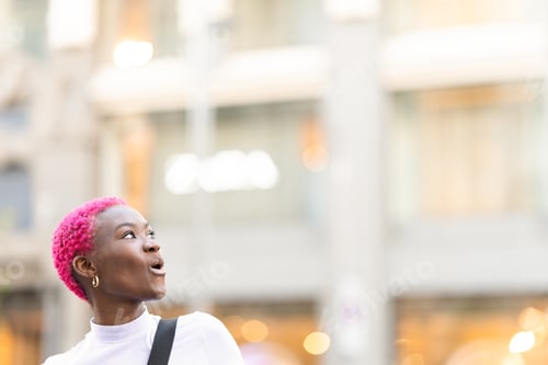 Preview: Photo with copy space of a young african woman looking up with surprised expression outdoors