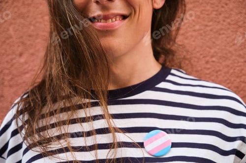 Preview: Close up of transgender woman with long hair and transgender flag pin.