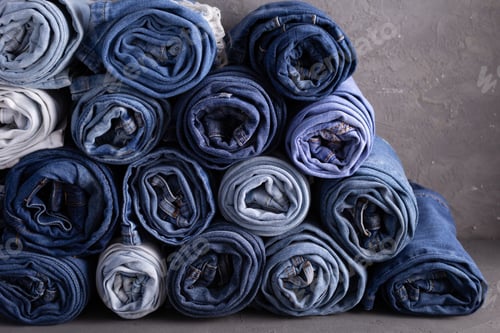 Preview: Blue jeans denim heap on table background. Jeans fabric heap as material surface
