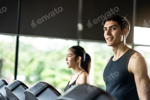Preview: Active young sport man and woman walking on treadmill or running machine in modern fitness gym.