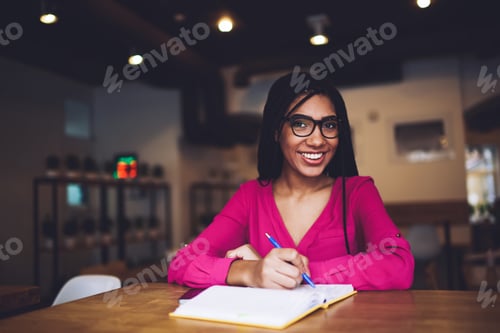 Preview: Delighted black woman writing notes in notepad