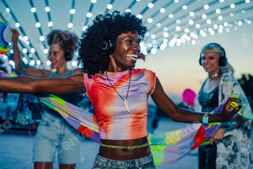 Preview: Happy friends listening music and dancing at silent disco party wearing headphones at sunset